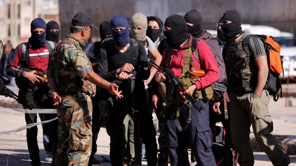 Los combatientes rebeldes llevan sus armas y pertenencias mientras hablan con un soldado del ejército sirio. Reuters