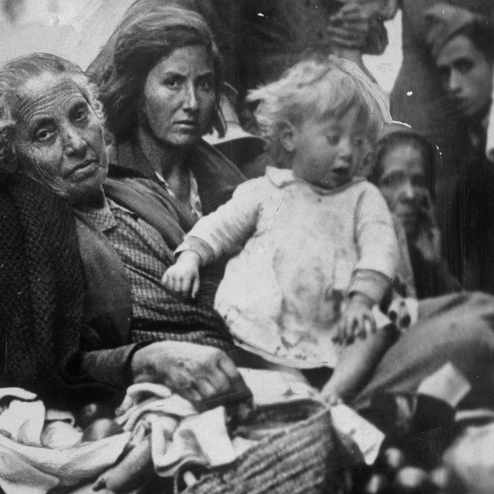 En 1937 los refugiados se contaban por miles en España, sumida en la guerra civil. Una anciana, junto a su hija y a su nieta, refugiadas todas de la guerra civil española, llegan a Valencia cargando sus pertenencias en 1937.