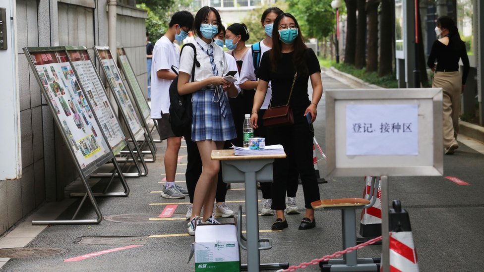 Masked students wait in a queue for their Covid jabs