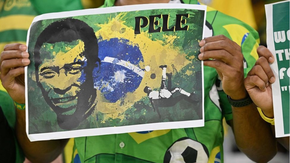 Um homem segurando um cartaz com o rosto de Pelé e a bandeira do Brasil