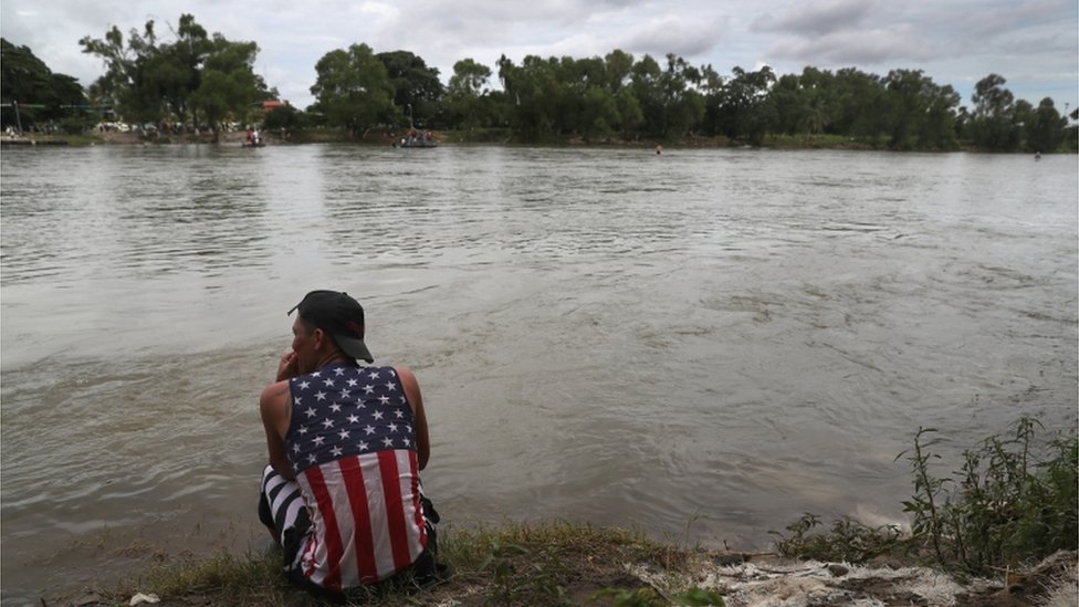 Migrante en la frontera con una camisa con la bandera estadounidense.