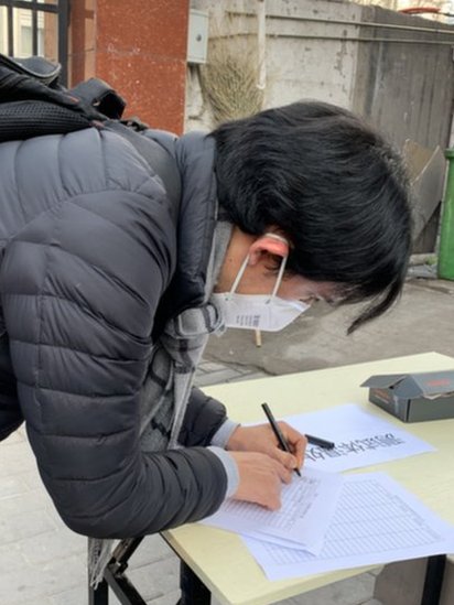 11 febrero 2020. Michael llenando sus datos y grado de temperatura en un registro fuera de un compound, en Pekín.