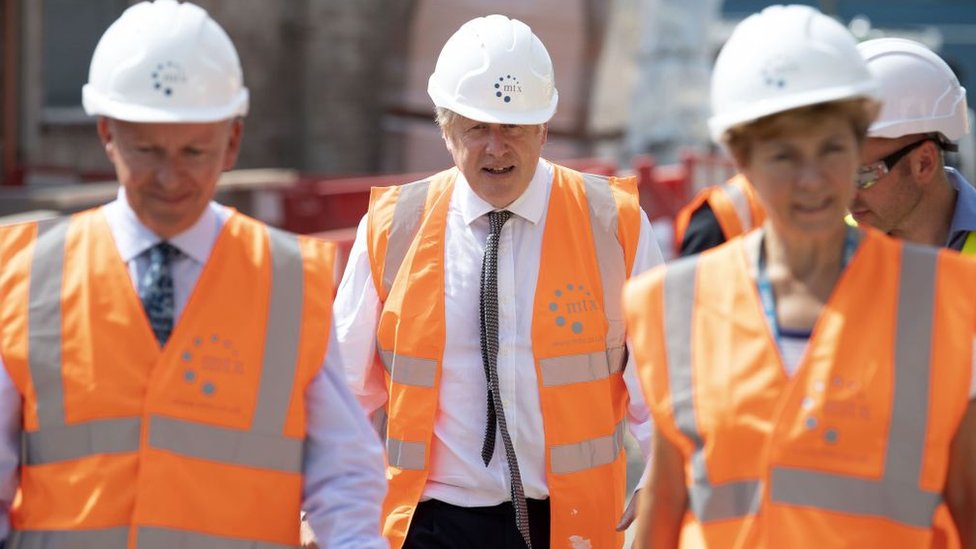 Boris Johnson wearing hi-vis and hard hat flanked by two others wearing the same.