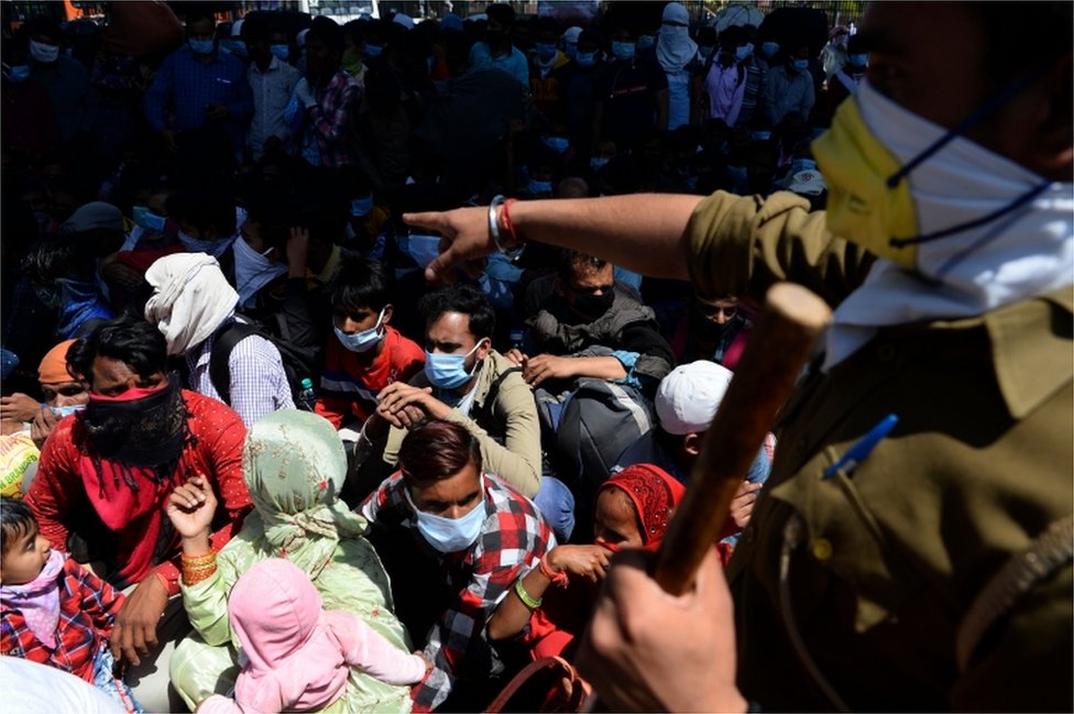 Офицер полиции инструктирует рабочих-мигрантов и членов их семей выстроиться в очередь, когда они покидают столицу Индии и отправляются домой во время общенациональной блокировки, введенной правительством, в качестве превентивной меры против коронавируса COVID-19
