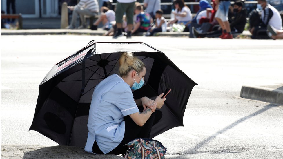 A woman uses an umbrella to shelter from the sun as she waits for a Coronavirus test outside a community centre following the outbreak of the coronavirus disease (COVID-19) in Bury