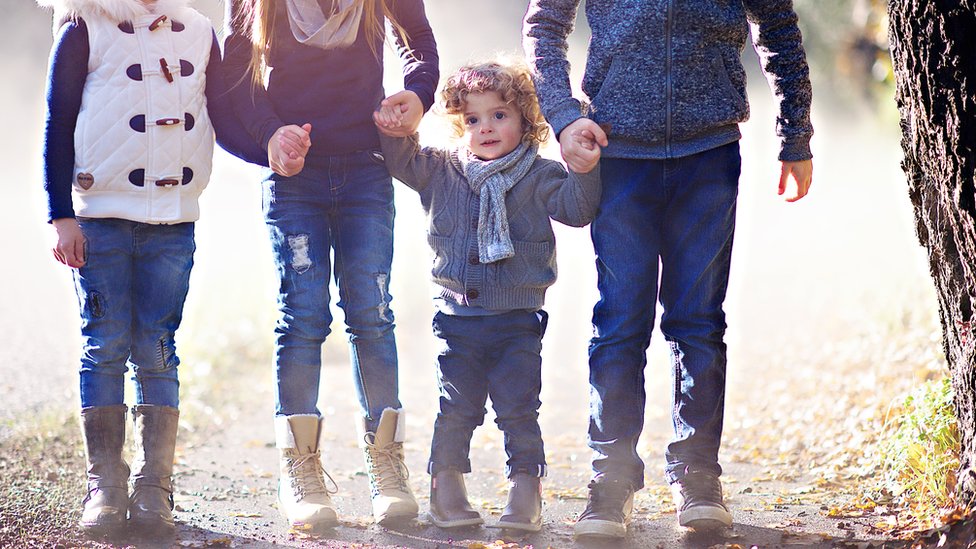 stock image of a little boy holding hands with his two older siblings, and a fourth child alongside