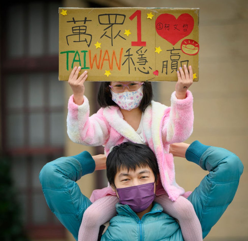 一名婦女舉起女兒，她的女兒舉著支持台灣民眾黨的標語牌