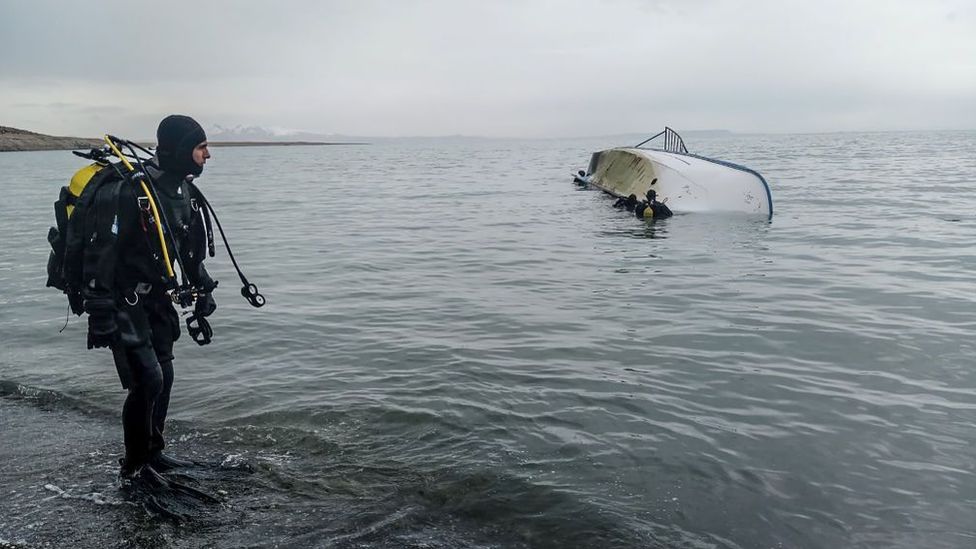 A diver looks at colleagues in the water by an overturned boat