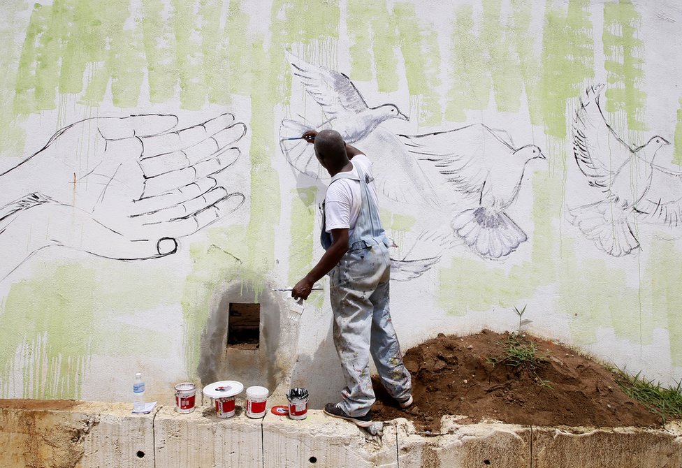 An artist stands on a step-ladder as he paints a pair of cupped hands reaching out to white doves.