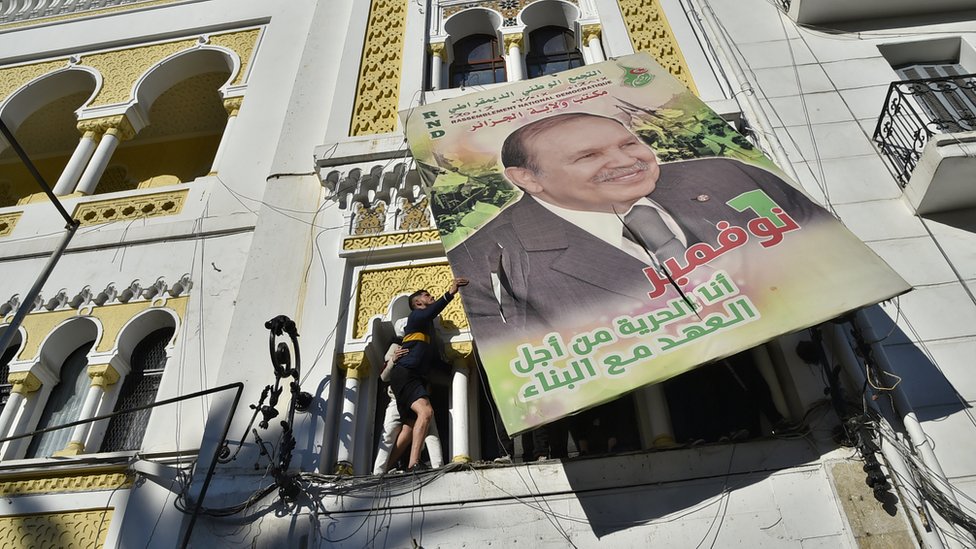 Алжирские демонстранты сносят большой рекламный щит с портретом бывшего президента Абдельазиза Бутефлика.