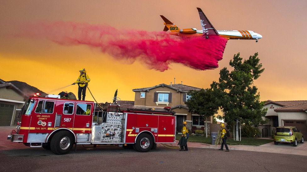 Самолет сбрасывает огнезадерживающие материалы позади домов вдоль McVicker Canyon Park Road на озере Эльсинор в США
