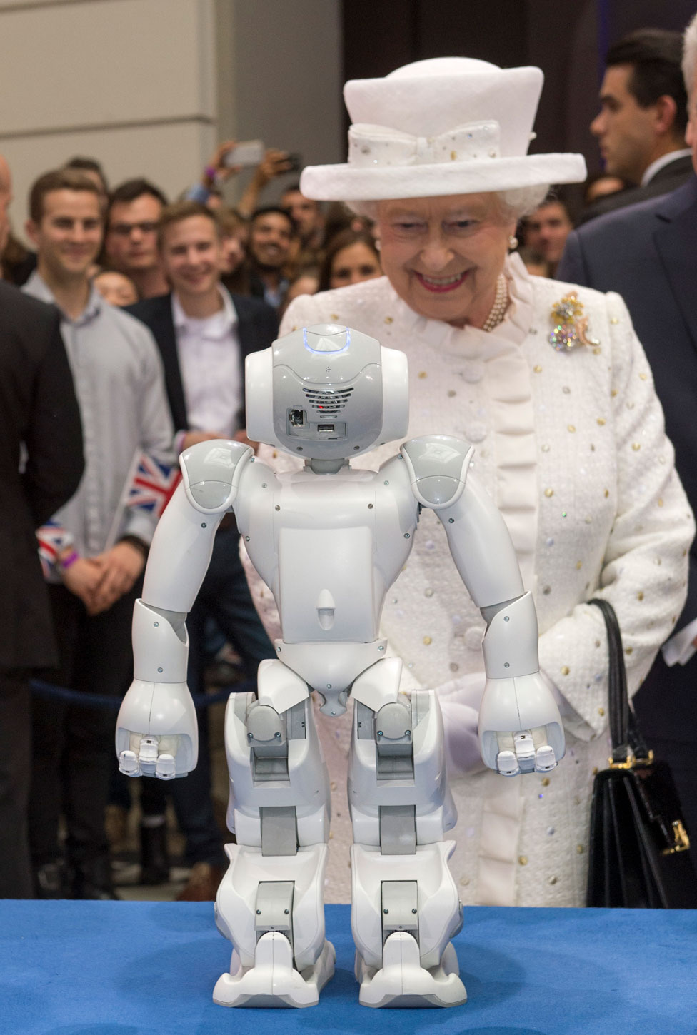 Queen in white hat looking at robot