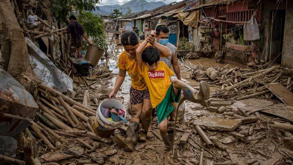 A child removes mud from his boot as residents wade across muddy floodwater and debris in a village after Typhoon Vamco hit on November 14, 2020 in Rodriguez, Rizal province, Philippines.