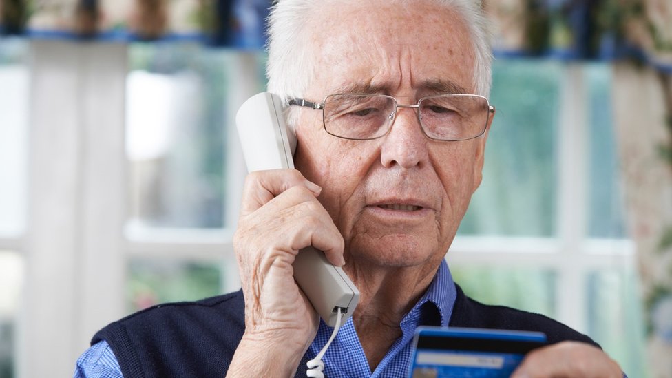 older man on phone with credit card in hand