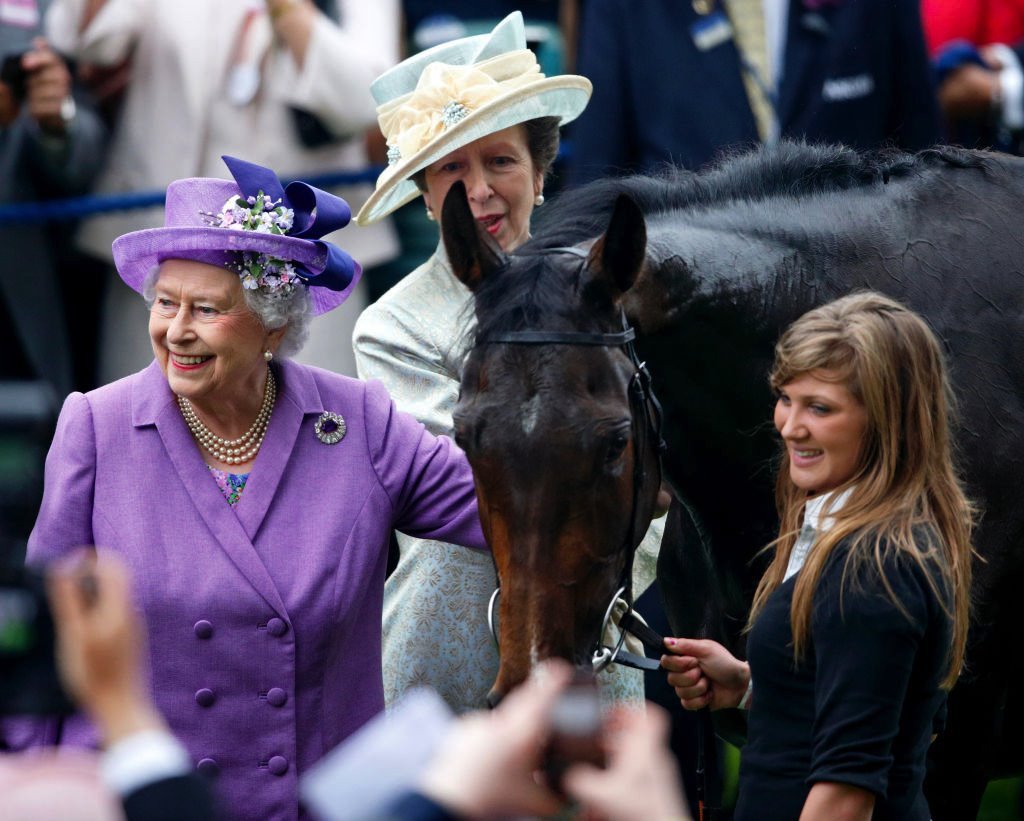 A rainha Elizabeth 2ª sorrindo ao lado de cavalo e de outras pessoas