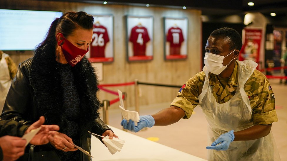 A member of the Royal Artillery hands a test to people at a testing centre at Liverpool Football Club's Anfield stadium