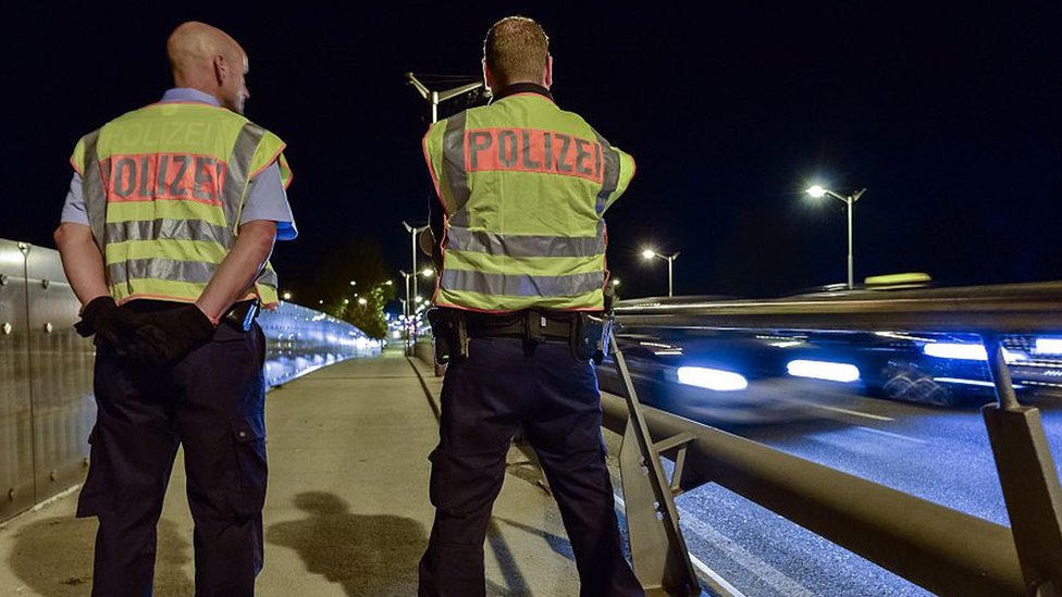 A photograph of German police officers standing by the side of a motorway at night