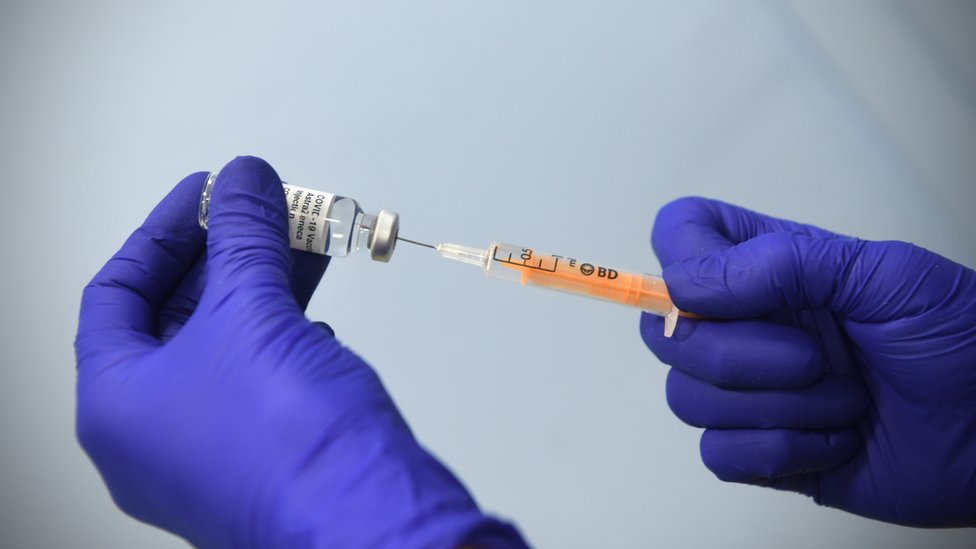 Gloved hands drawing AstraZeneca vaccine from a vial with a syringe