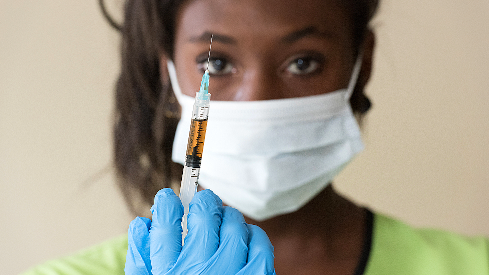 Типичное фото медсестры в маске, держащей вакцину