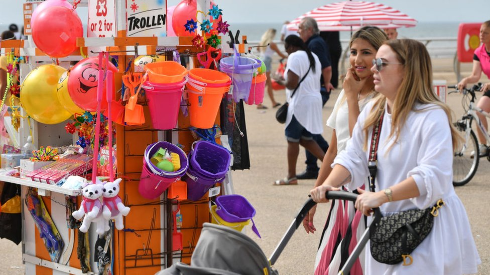 Two women walk past a stall selling toys on a beach