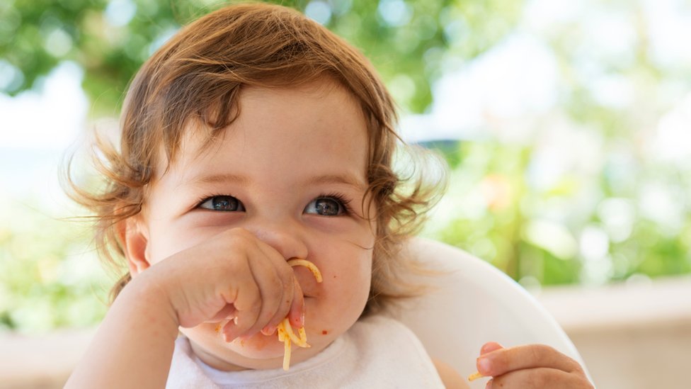 Niña comiendo fideos con la mano