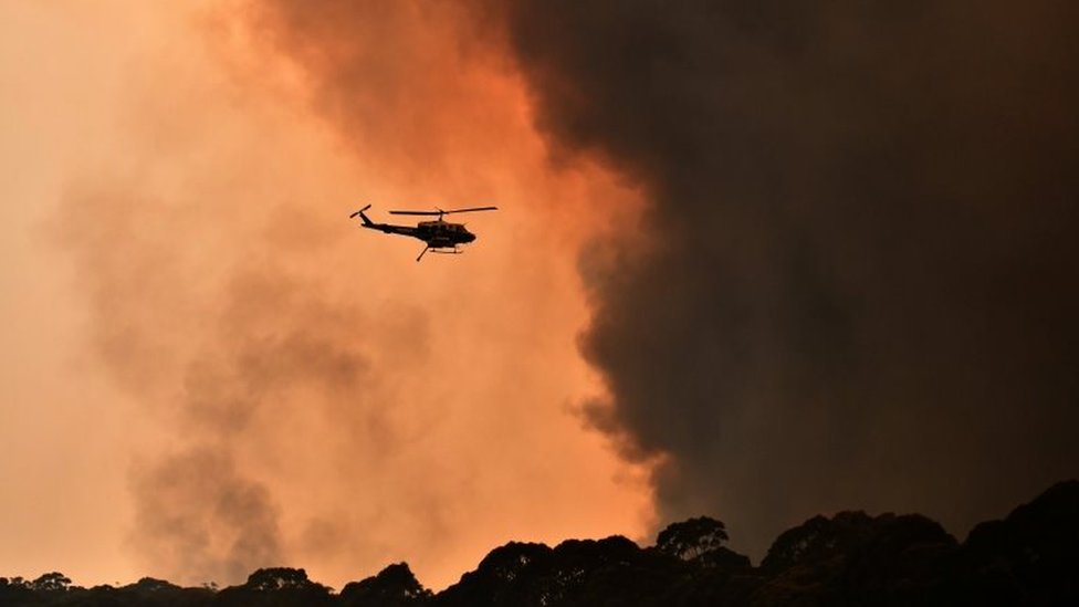 Вертолет пролетает мимо черного дыма от лесного пожара
