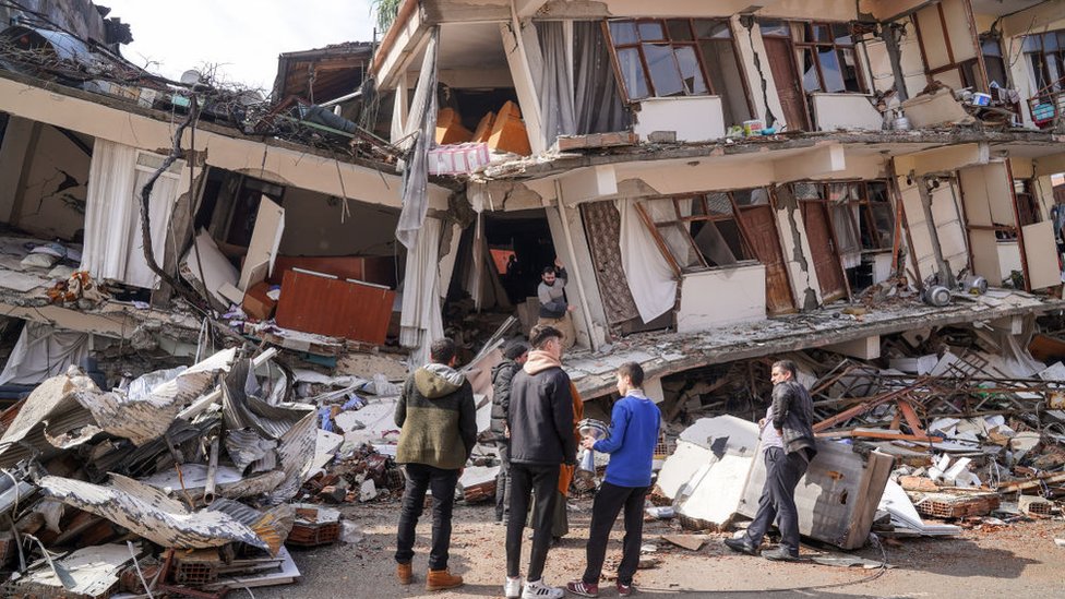 A group of people look at their destroyed apartment building.