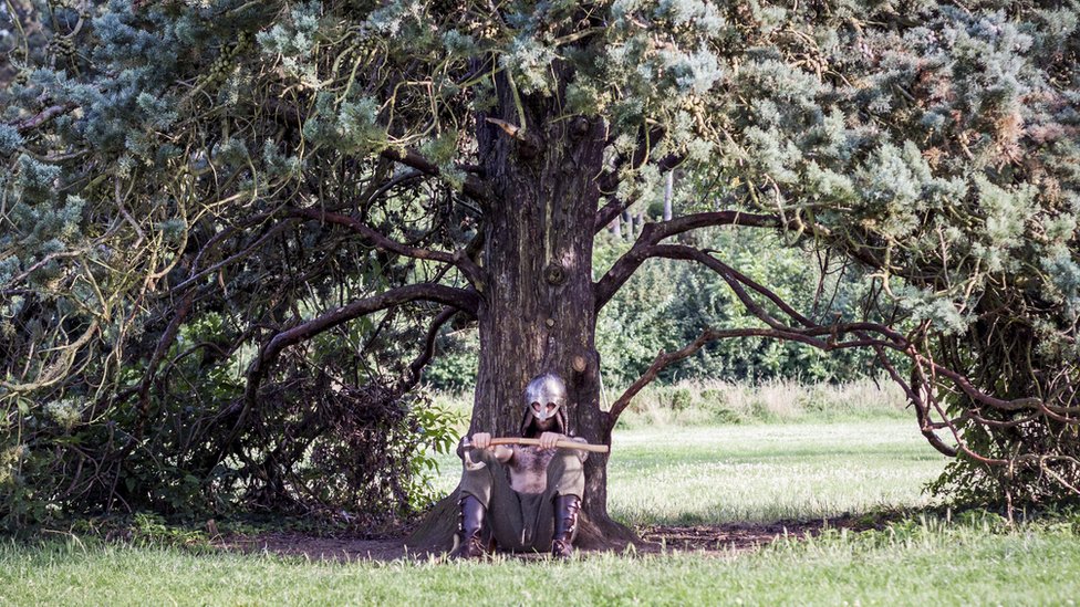 A man dressed as a Viking laying under a tree.