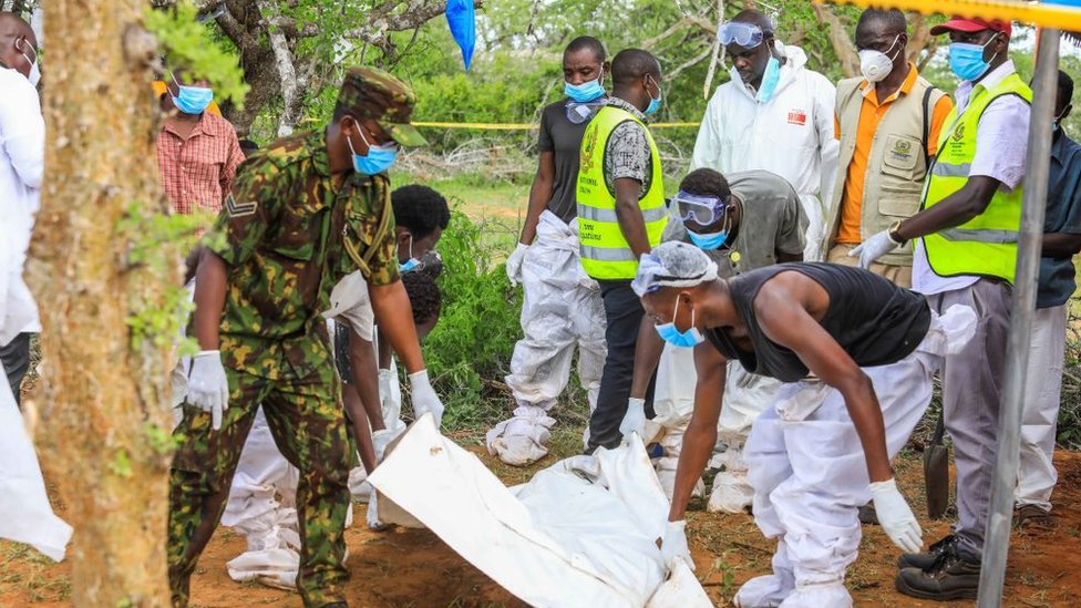 Officials carry a dead body of a person who died in Kenya's starvation cult near the Good News International Church in Malindi town of Kilifi,