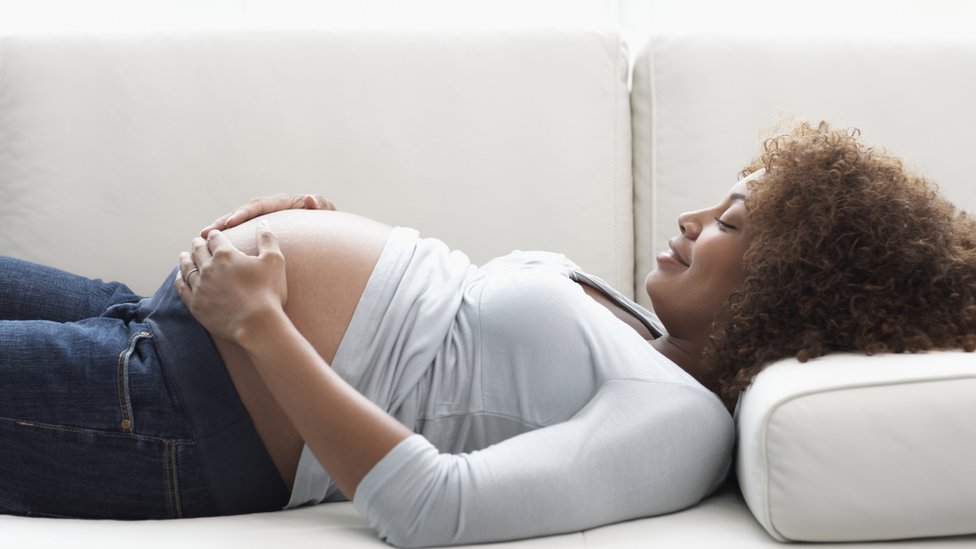Una mujer embarazada acostada en un sofá se toca su barriga