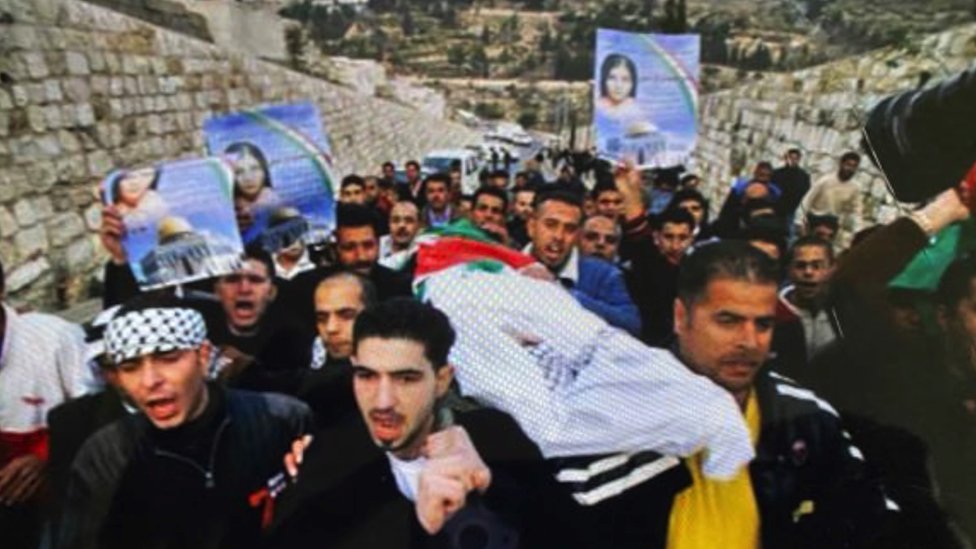 Mourners at the funeral for Bassam's daughter, holding pictures of her