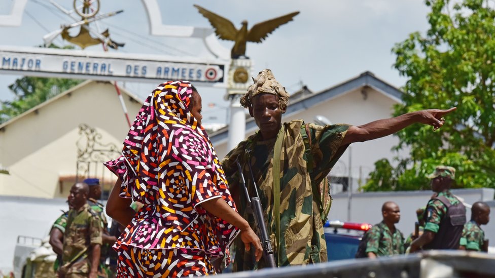 Солдат-повстанец жестом стоит у входа в штаб-квартиру армии Кот-д'Ивуара, военный лагерь Галлиени, в Абиджане 12 мая 2017 года, когда они стреляют в воздух всего через несколько часов после того, как представитель протестующих публично извинился за более ранний мятеж.