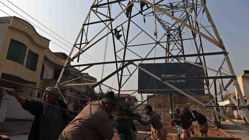 Pakistani electricity workers pull a rope as they complete a high voltage power pole in Rawalpindi on 29 December 2014