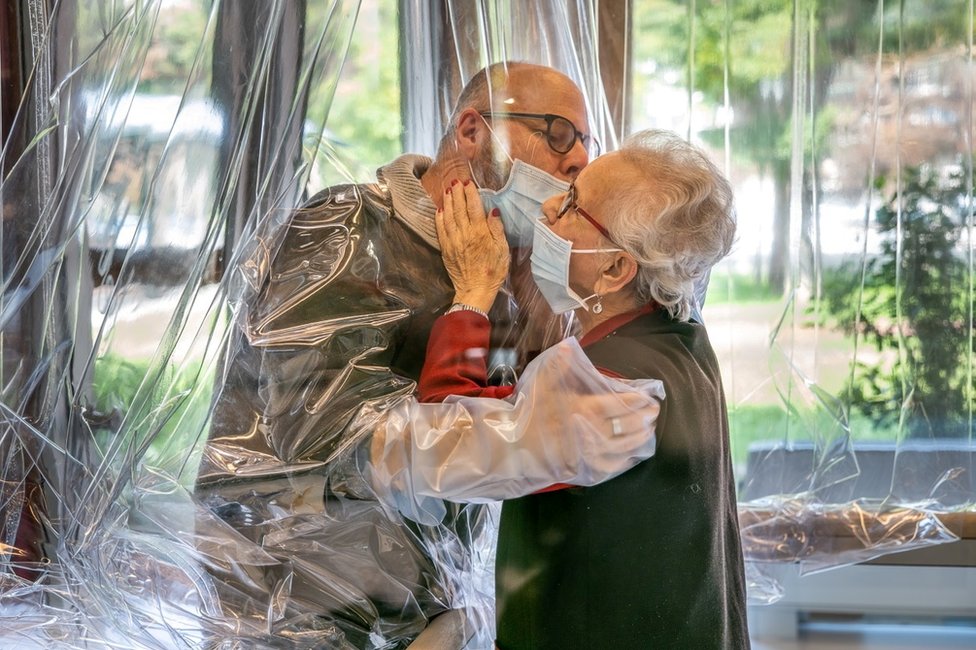 A care home resident kisses their relative through a plastic sheet