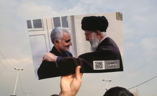 Kasım Süleymani ve Ayetullah Ali Hameney'in birikte çekilmiş bir fotoğrafını taşıyan İranlı gösterici