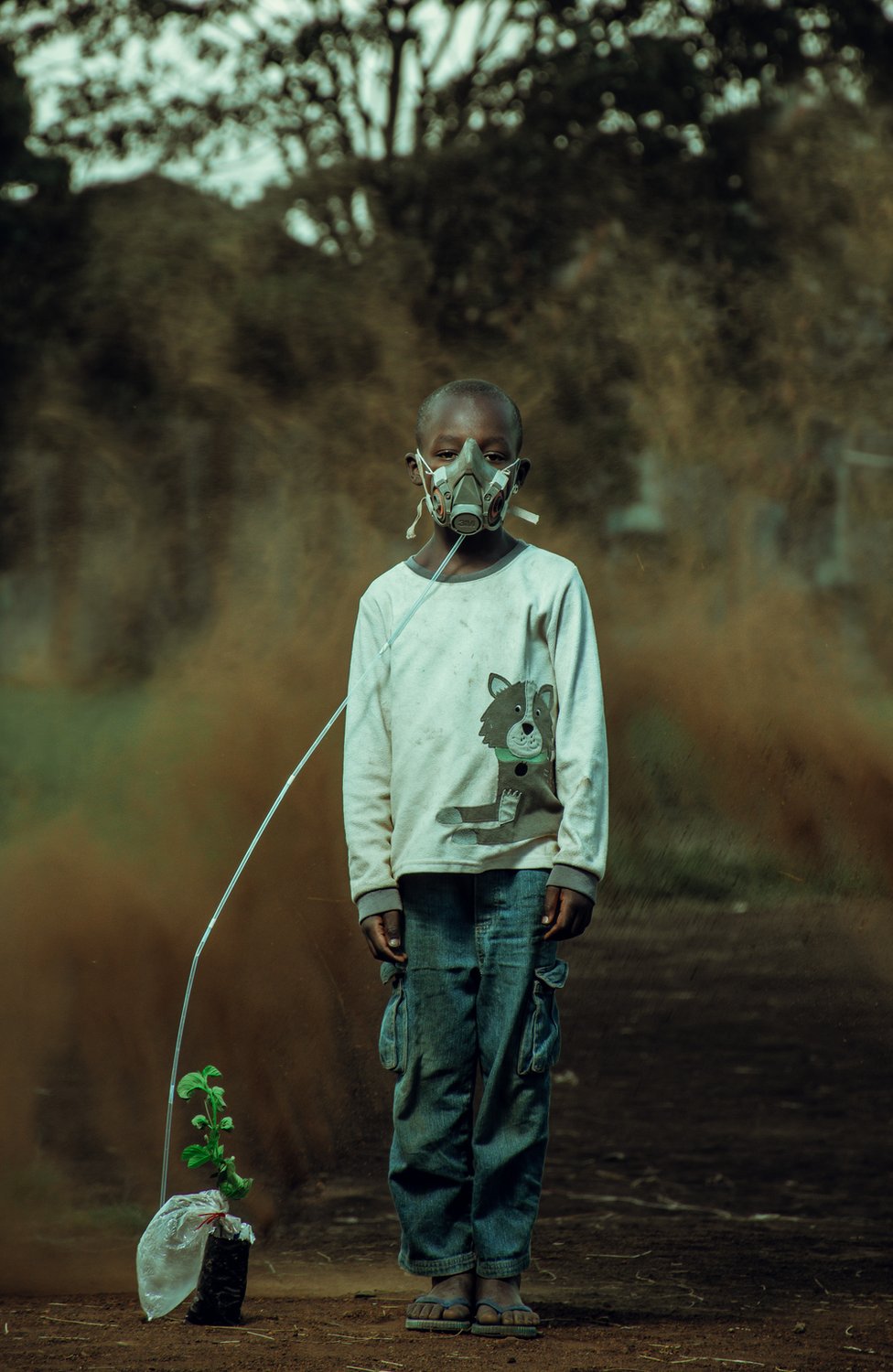 Un niño con una máscara de oxígeno conectada a una planta, con una tormenta de arena en el fondo