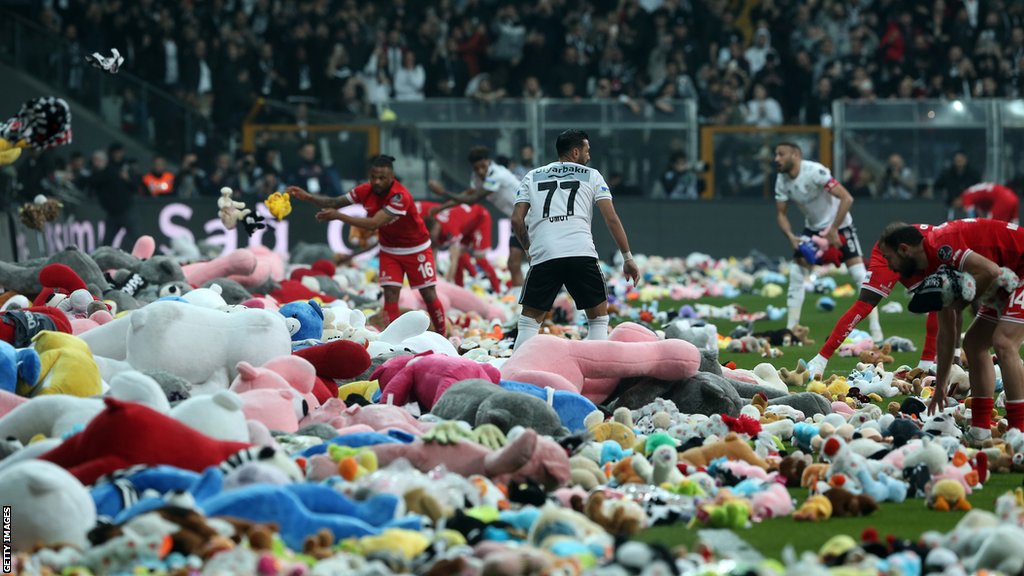 Players remove Teddy bears from the pitch, thrown on to the field in support for the earthquake victim children