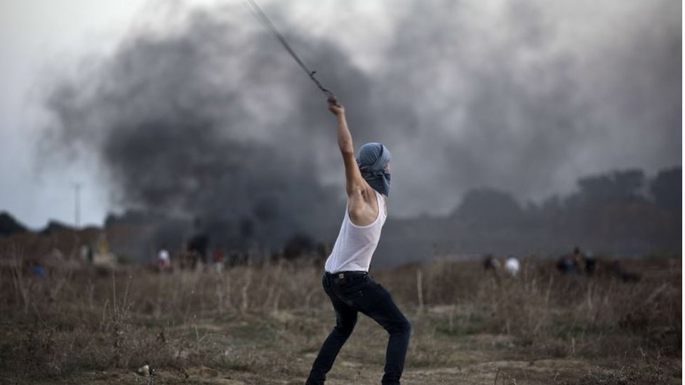 Палестинский демонстрант использует рогатку, чтобы бросать камни в израильских солдат во время столкновений у пограничного забора между Израилем и центральной частью сектора Газа к востоку от Бурейджа 15 октября 2015 года.