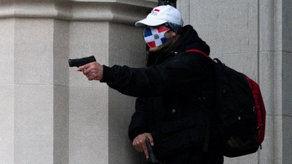 Фотография Reuters, на которой изображен боевик с двумя пистолетами и в маске с изображением флага Доминиканской Республики