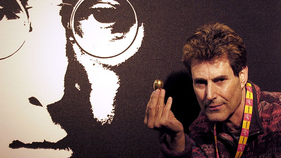 Uri Geller with an egg-shaped object in front of picture of John Lennon (2005)