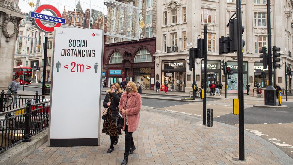 People wear masks next to a social distancing sign in London's Oxford Circus