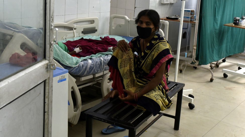 Hindistan'da bir hastanede yakının yanında oturan bir hasta yakını.