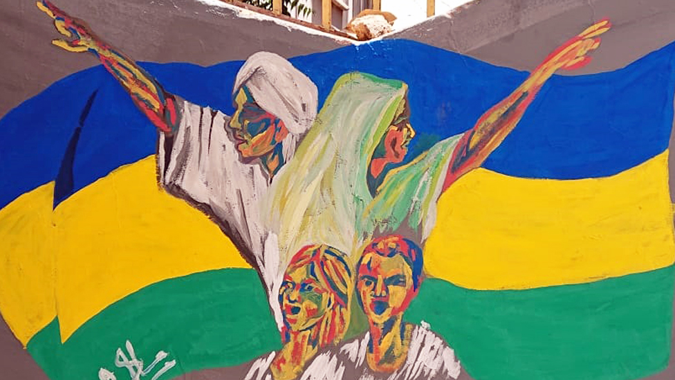 رجل وامرأة وطفلان في جدارية خلفيتها العلم السوداني، الخرطوم