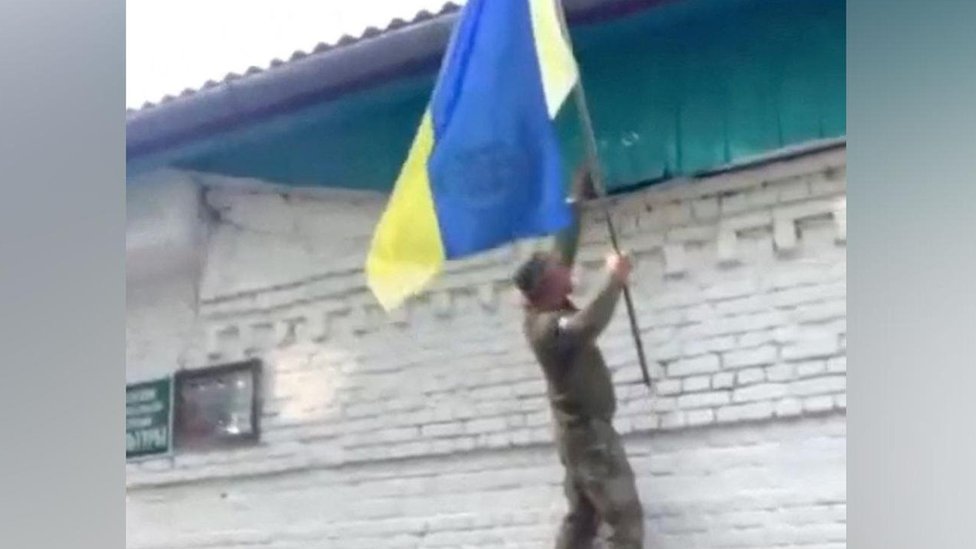 A Ukrainian soldier placing a national flag on a building in a Russian village.