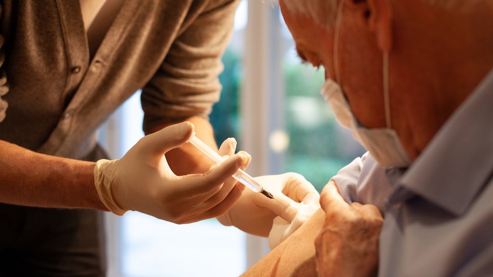 Pessoa aplica vacina em idoso