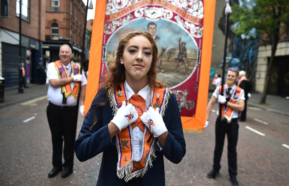 Молодая женщина в кушаке Ордена Оранжистов, а за ней двое Оранжистов несут знамя
