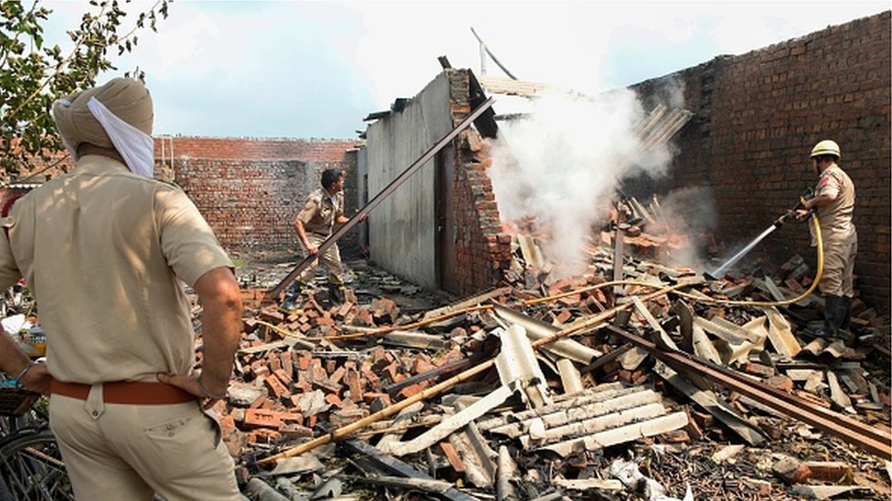 A police officer looks on while fireman douses a fire after an explosion at a cracker factory on the outskirts of Amritsar on August 2020