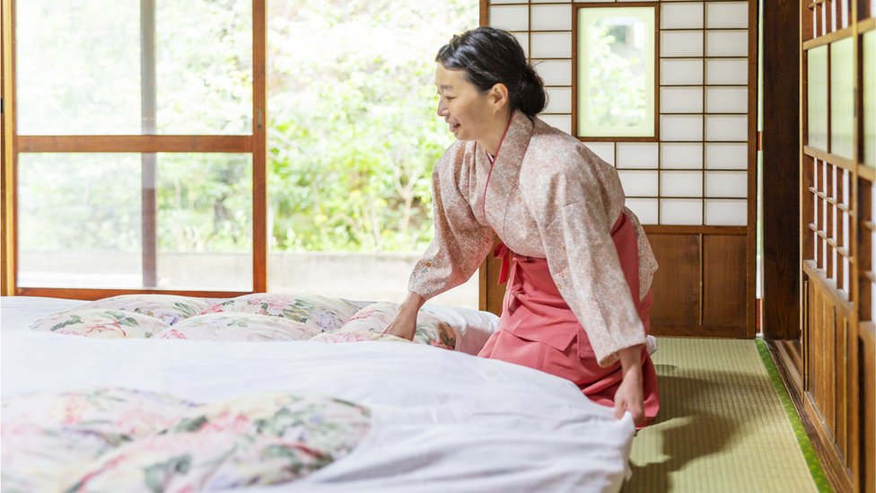 An oriental woman prepares a futon.