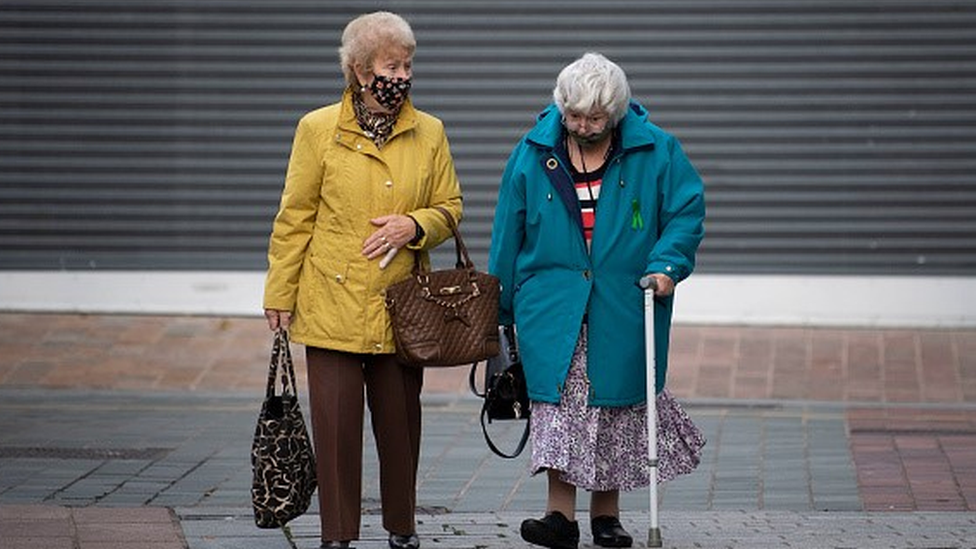 Duas idosas de máscara caminham pela rua