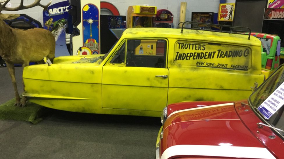 Копия автомобиля Del Boy Reliant Robin с тремя колесами. На желтой машине есть логотип торговой марки Trotters Independent Trading Co.